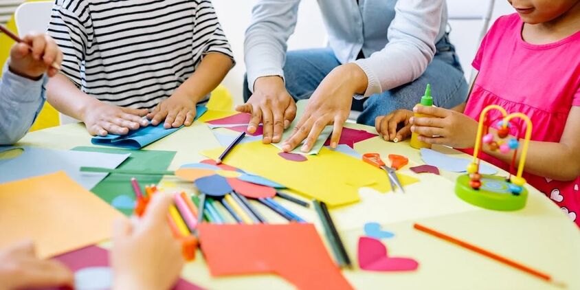 Image d’une assistante maternelle avec des enfants, autour d’une table pour enfants, en train de jouer.